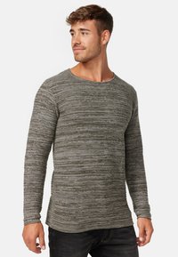 Szary w paski longsleeve z okrągłym dekoltem, wykonany z teksturowanej tkaniny. Wzór składa się z naprzemiennych cienkich i grubych pasków.