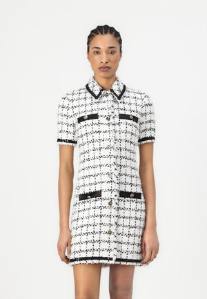White and black tweed dress with short sleeves, collar, front pockets, gold buttons, and contrasting trim detailing. Textured fabric with a classic pattern.