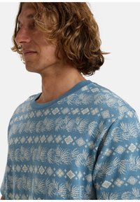 Short-sleeve blue shirt featuring a white floral and geometric pattern, with a round neck and soft texture.
