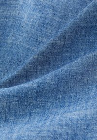 Gros plan sur un tissu en denim bleu texturé avec un motif de tissage visible et des plis naturels créant des ombres et des reflets.