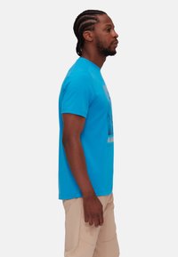 Blå bomulls t-shirt med grafiskt tryck och korta ärmar, med avslappnad passform. Bärs tillsammans med ljusa cargoshorts.