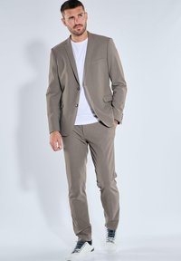 Light brown suit made of smooth fabric, featuring a single-button blazer and tapered pants, paired with a white t-shirt and white sneakers.