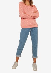 Sudadera rosa con estampado de pájaros blancos, cuello redondo y puños acanalados, combinada con vaqueros azules remangados y zapatillas blancas.