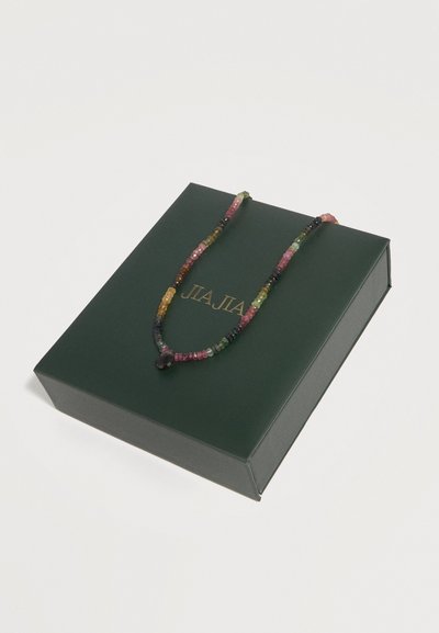 Collier multicolore en perles avec un pendentif sombre affiché sur une boîte rectangulaire vert foncé avec des lettres dorées.