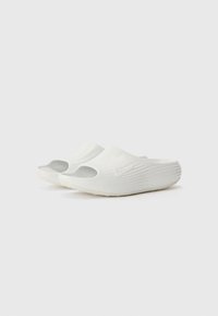 White Nike sandals with open toe, curved design, textured ridges on sides, and a flat sole. Features a small logo on the side.