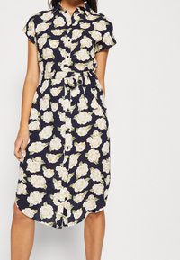 Blommig skjortklänning med korta ärmar, marin bakgrund, stort mönster av vita rosor, knytning i midjan och rundad nederkant.