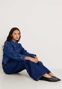 Két első zsebbel ellátott farmerdzseki, bő szárú farmernadrággal párosítva; fekete, ezüst díszítésekkel ellátott hegyes orrú balerinacipő.