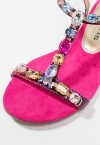 Světlé růžové sandály s multikolorovými ozdobami z drahokamů na tmavých strukturovaných popruzích a semišovou stélkou.