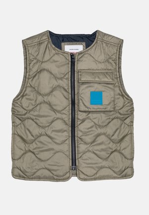 Ærmeløs beige quiltet vest med lynlås foran, en brystlomme med klap og en blå firkantet lap på højre brystområde.