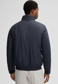 Navyblauwe gewatteerde jas met een hoge kraag, elastische zoom en manchetten. Gladde textuur, eenvoudig ontwerp, geen zichtbare patronen of hardware.