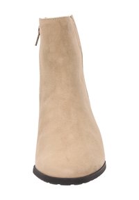 Bottines en suede beige avec une texture lisse, une fermeture éclair sur le côté et une semelle en caoutchouc noire basse. Design simple et moderne.