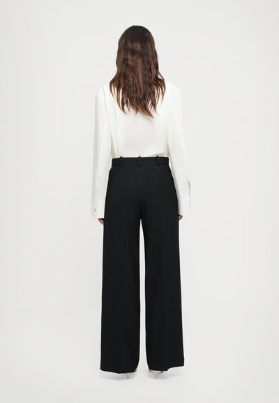 White long-sleeve blouse paired with black high-waisted wide-leg trousers. The blouse features buttoned cuffs; trousers have a back pocket.