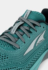 Aqua mesh träningssko med grå skosnören och en grå logotypetikett, med en lätt design och texturerad yta för andningsförmåga.