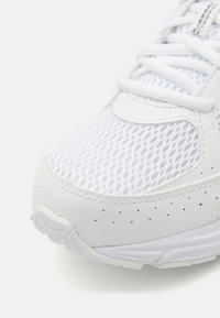 Scarpa sportiva bianca con upper in mesh, dettagli in pelle testurizzata e lacci tonali. Include dettagli perforati per la traspirabilità.