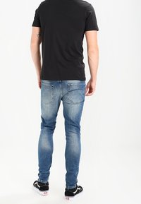 Svart kortärmad t-shirt, ljusblå slim-fit jeans med fem fickor och svarta sneakers med vita sulor. Minimal branding synlig.