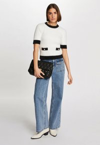 Suéter blanco de manga corta y peludo con ribete negro y bolsillos de parche, combinado con pantalones vaqueros de pierna ancha de color azul claro y un bolso clutch acolchado negro.
