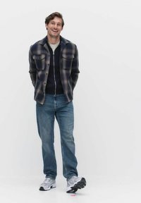 Rutigt skjorta i marinblått och grått, lager på lager över en marinblå zip-up, kombinerat med ljusblå jeans och grå sneakers. Enkelt design, avslappnad passform.