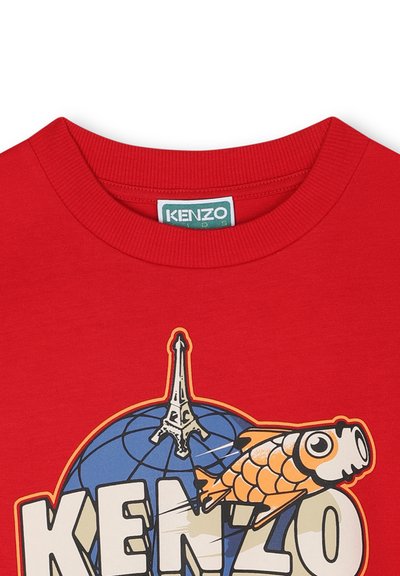 T-shirt en coton rouge avec un design graphique représentant un globe, une silhouette de la Tour Eiffel et un poisson orange, ainsi que le nom de la marque "KENZO."