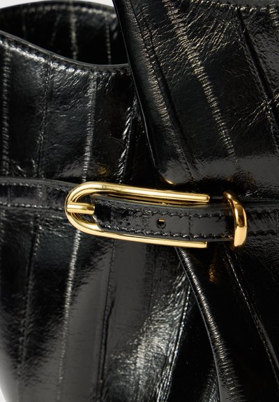 Zwarte leren tas met een glanzende afwerking, voorzien van een gouden gespaccent en textuurlijnen op het oppervlak. Close-up van de band en bevestigingsdetail.