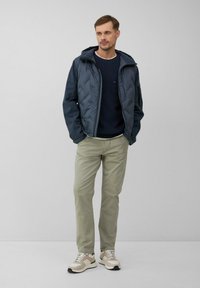 Granatowa pikowana kurtka z kapturem, zestawiona z ciemnoniebieskim swetrem, jasnozielonymi spodniami oraz beżowymi trampkami z zielonymi akcentami.