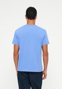 Rövid ujjú kék pamut póló, kerek nyakkal, sima textúrával és egyenes szegéllyel, hátulról nézve.