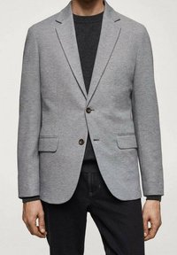 Blazer grigio chiaro realizzato in tessuto testurizzato, con chiusura a due bottoni, rever a punta e due tasche frontali, abbinato a una parte superiore scura.