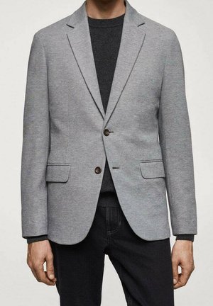 Hellgrauer Blazer aus strukturiertem Stoff, mit einem Zwei-Knopf-Verschluss, Reverskragen und zwei vorderen Taschen, kombiniert mit einem dunklen Oberteil.