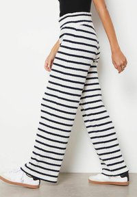 Pruhované široké kalhoty s ribovanou texturou, s vodorovnými námořnickými a bílými pruhy, vysokým pasem a nošené s bílými teniskami.