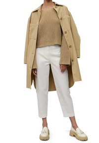 Un manteau oversize beige, un pull en maille texturé beige, un pantalon blanc et des mocassins crème avec une semelle épaisse et des accents de détails.