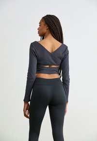 Dark gray ribbed long-sleeve top with a V-back design, paired with high-waisted black leggings. Features cut-out detail at the back.