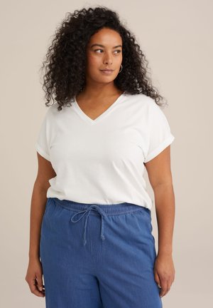 White loose-fitting V-neck t-shirt with rolled short sleeves, paired with blue elastic waist trousers featuring a drawstring. Smooth fabric texture.