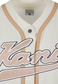 Jersey crema con righe verticali, dettagli beige e chiusura con bottoni. Presenta il logo ricamato "Kani" in nero e beige.