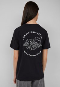 Czarna bawełniana koszulka z krótkim rękawem, z białymi grafikami i napisami z tyłu, w tym wzorem precla i hasłami.