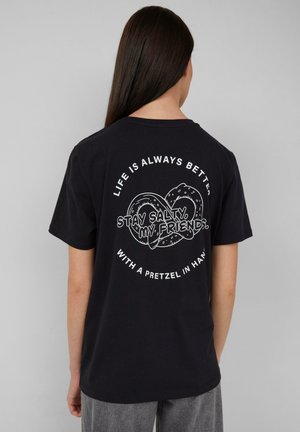T-shirt en coton noir avec un texte graphique et des illustrations blanches au dos, y compris un design de bretzel et des slogans. Manches courtes.