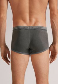 Szare slipy w bokserskim stylu z płaskim pasem na którym znajduje się logo marki. Gładki materiał i dopasowany fason z krótkimi nogawkami oraz przylegającym krojem.