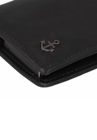 Zwarte leren portemonnee met een metalen ankerlogo, contrasterende stiksels, een gladde textuur en een rechthoekig, slank ontwerp.