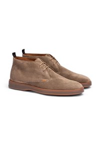 Bottines chukka en daim marron avec une semelle en caoutchouc tan lisse, un design à lacets et des accents de talon contrastants. Présente un minimum de couture et des lignes épurées.