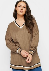 Suéter de punto marrón de manga larga con un patrón texturizado, cuello en V con rayas en blanco y negro en contraste, y un corte oversize.