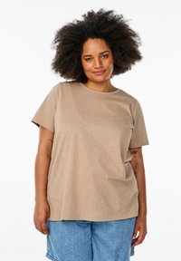 T-shirt beige à manches courtes avec un col rond, présentant une texture à pois. Porté avec un short en denim bleu clair.