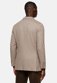 Blazer marrón de espiga con un corte ajustado, abertura simple y puños de dos botones. Textura suave con un patrón sutil, tela ligera.