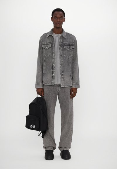 Veste en jean grise avec fermeture à bouton et deux poches avant, associée à un pantalon gris. Sac à dos noir avec le texte "ICON". Chaussures noires.