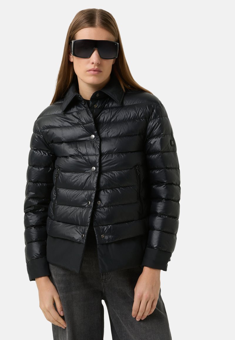 Schwarze Steppjacke mit glänzendem Finish, mit Kragen, Reißverschlusstaschen und silbernen Druckknöpfen. Gestylt mit übergroßen Sonnenbrillen.