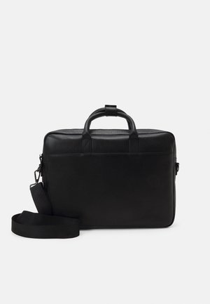 Mallette en cuir noir avec poignées supérieures et bandoulière amovible sur un fond clair uni.