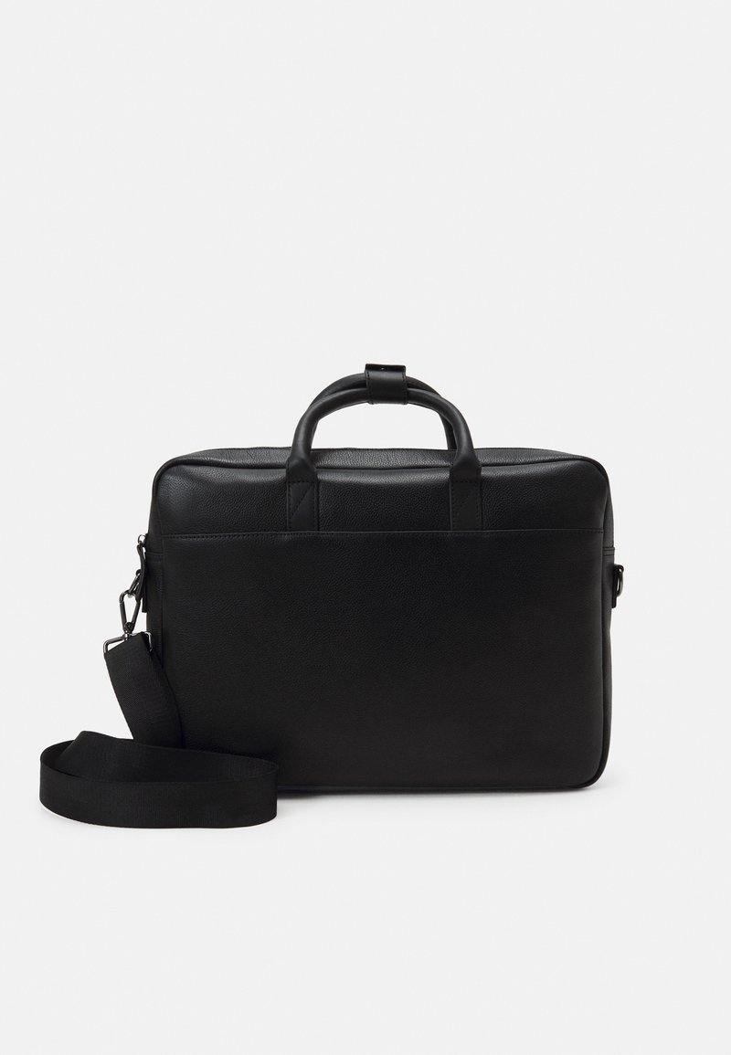 Mallette en cuir noir avec poignées supérieures et bandoulière amovible sur un fond clair uni.