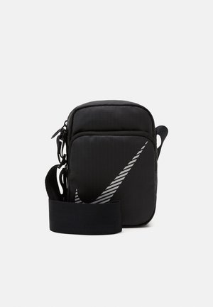 Borsa a tracolla nera in nylon con cintura regolabile, caratterizzata da un grande logo Nike swoosh grigio e una chiusura con zip. Superficie texture.