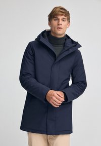 Parka blu navy con cappuccio e chiusura zip, dotata di una fodera interna testurizzata. Il design include tasche laterali e una silhouette elegante.