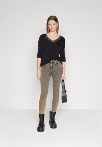 Zwarte lange mouwtop met kanten rand, gecombineerd met vervaagde lichtbruine skinny jeans en zwarte veterboots. Houdt een zwarte riem vast.