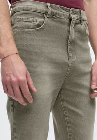 Šviesiai rudos spalvos džinsai tiesaus kirpimo, su klasikinio penkių kišenių dizainu, subtiliu išblukimu ir užtrauktuku priekyje.