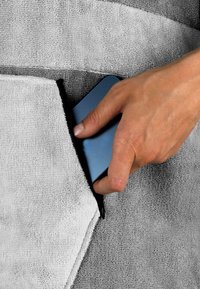 Ein graues Handtuch mit einer Tasche, das ein blaues rechteckiges Objekt hält. Der Stoff hat eine strukturierte, geschlungene Webart.