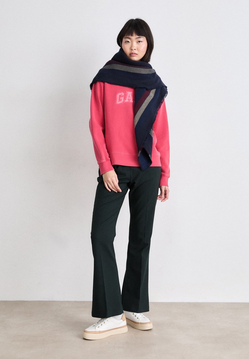 Różowy sweter z logo "GAP", zielone spódnice w kształcie dzwonu, ciemnoniebieski szalik w paski i białe trampki na platformie. Gładkie materiały i luźny krój.
